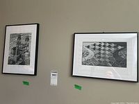 Two black and white framed prints hanging on a wall. The left print shows a surreal architectural waterworks scene, the right print shows a pattern of birds forming shapes over a landscape.
