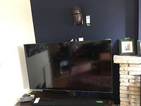 Front view of Samsung flat screen TV on pedestal stand with cables visible.