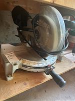 Front angled view of Delta miter saw showing the blade guard, measurement scale, and handle, placed on a wooden shelf.