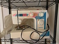 Front left side view of White Jeans Machine sewing machine on metal shelving, showing overall condition and attached power cord.