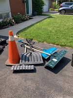 Group photo showing four snow shovels and one orange traffic cone in driveway, use wear visible.