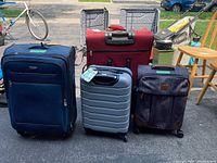 Photo shows four suitcases: One small silver hard-shell, one medium red softshell, one large navy blue softshell, and one medium gray fabric suitcase with leather accents and wheels.