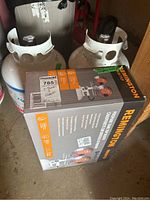 Two 20-lb propane tanks beside boxed Remington heater