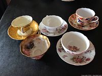 Overview of 5 tea cups and saucers from various English bone china makers showing different floral and gold designs.