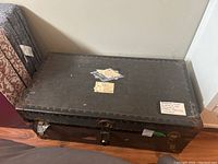 Front, top, and side angled view of the black vintage card steamer trunk showing metal corner protectors, metal lock, and travel stickers on the top surface.