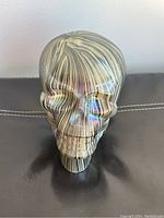 Front view of iridescent glass human skull figurine showing detailed facial features and striped pattern
