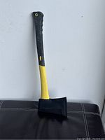 Full view of the 24in camping axe leaning against a wall, showing the black and yellow handle and the covered steel head.