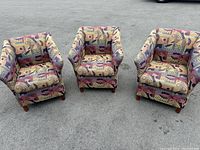 Three Clou chairs arranged on pavement showing front view, colorful geometric upholstery and wood legs with casters.