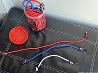 Photo of red, blue, and white elastic straps with black metal hooks spread out on a black leather surface, with a clear plastic container next to them.