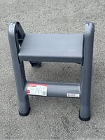 Gray Rubbermaid folding step stool shown folded on a gray pavement background.