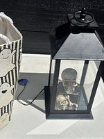 Photo showing black metal lantern with skull and bone decorations inside and LED light cord visible