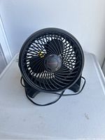 Black Honeywell fan front view showing circular grill and three blades inside, cord attached