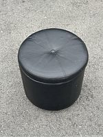 Top and side view of black leather-like cylindrical ottoman showing stitched top surface and slight wear marks.