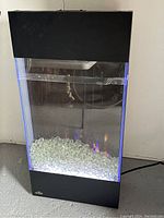 Front view of Napoleon Allure Vertical 32 electric fireplace on floor, black frame with glass front, crystal ember bed illuminated with blue LED light and visible flame effect.