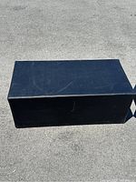 Black rectangular upholstered seat bench shown on pavement, top and side views visible.