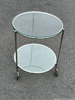 Front and side view of the stainless steel pedestal table showing two round glass trays and wheels.