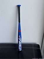 Blue Rawlings alloy T-ball bat standing upright against a white wall, showing full length and details.