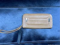 Front view of the brown leather Tahari wristlet wallet placed on a black surface, showing the Tahari logo and zipper closure.