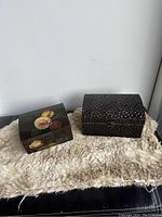 Two vintage decor boxes on a textured beige and black surface, showing front and side views.