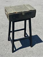 Full photo showing the vintage military style table box on black wooden stand outdoors on pavement.