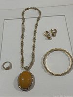 Photo showing entire jewelry set: necklace with large amber pendant, bangle bracelet, ring, and clip-on earrings arranged on a flat surface.