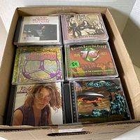 Box of assorted used CDs showing the top layer with various albums including Good Morning Vietnam soundtrack, Boston 'Hell on Heels', Psychedelic Psunday, Rolling Back the Years Seventies compilation, Ricky Martin, and The Rolling Stones Greatest Hits.