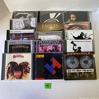 Top down photo showing 15 CD cases arranged in rows, various artist titles visible including Heart, Eagles, Jefferson Airplane, Bryan Adams and others.