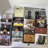 Photo showing variety of used CDs from various artists including Eric Clapton, Tragically Hip, Kid Rock and more arranged on white surface