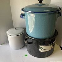 Two enameled canning pots stacked, blue pot on top and black pot below, with white kitchen canister beside them.