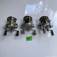 Three vintage Pflueger reels shown from front with varied handle colors and fishing line on spools.