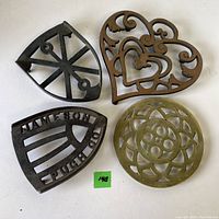 Top view of 4 different metal trivets arranged in a square on white background.