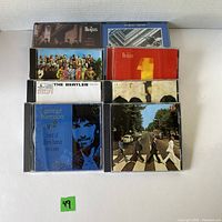Photo displaying 8 CDs including 7 Beatles albums and 1 George Harrison album arranged in 2 rows on white background.