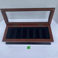 Open view of wooden watch case showing six black fabric-lined compartments and glass top lid