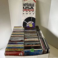 Photo showing a box filled with around 190 CDs arranged vertically, visible album titles including hits collections, DJ Network albums, and Adele CDs.