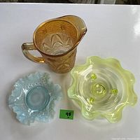Photo front view of amber carnival glass pitcher, blue ruffled edge bowl, and yellow translucent wavy rim bowl with glass prunts