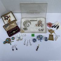 Entire jewelry lot displayed with vintage watch, rhinestone brooches, Christmas pins, and multiple pairs of earrings arranged on a flat surface.