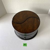 Top view of the closed round wooden jewelry box with dark wood grain and two crescent-shaped lids.