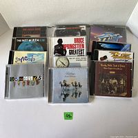 Photo showing a collection of 15 music CDs from various classic rock artists arranged in rows with visible album covers and band names