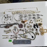 Top-down image of assorted costume jewelry displayed on a white surface showing various necklaces, earrings, brooches, bracelets, and hair accessories.