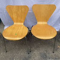 Front view of two wooden Mid Century style chairs with chrome metal legs on pavement with white backdrop.