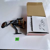 Photo of Sougayilang fishing reel with box and instruction manual from above, reel placed beside the box with instruction sheet partially inside box.