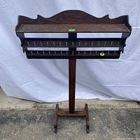 Front view of vintage wooden sewing spool holder with two rows of pegs and top storage shelf.