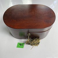 Top flat view of the wooden oval trinket box closed with key and tassel in lock.