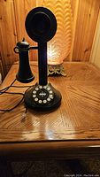 Full view of the black antique style candlestick telephone showing handset on hook and cord for connection.