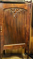 Front view of the antique wood cabinet door showing decorative scroll carving and wood grain with minor marking on the surface.