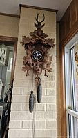 Full front view of wall-mounted carved wood cuckoo clock with stag head and pinecone weights