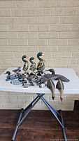 Wide view of all duck figurines arranged on white folding table against brick wall background