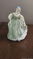 Full side view of Royal Doulton Fair Maiden porcelain figurine showing green dress, cream sleeves, blue bow in hair.