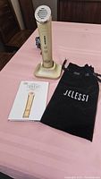 Jelessi Torch+ skin enhancer device on charging base, user manual, and black pouch on pink surface