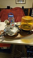 Photo of a frying pan with glass lid, yellow popcorn maker, blue handled jug, and white ceramic mugs on a table.